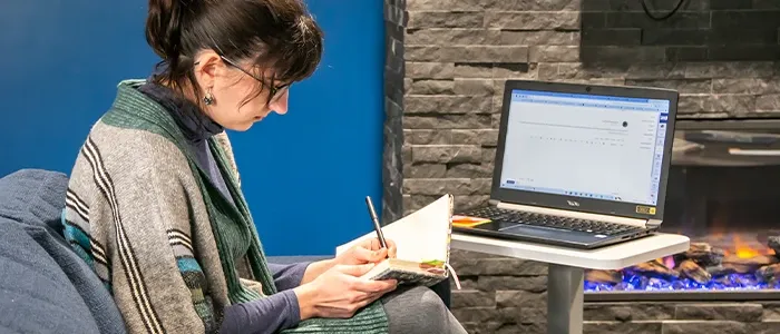 a student journals in front of her laptop in a student common area